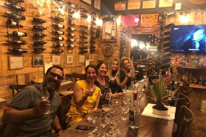 A group of people seated at a table in a wine cellar with numerous wine bottles on the walls. 4
