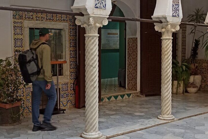 A man walking past a building with a patterned facade and a green door. 5