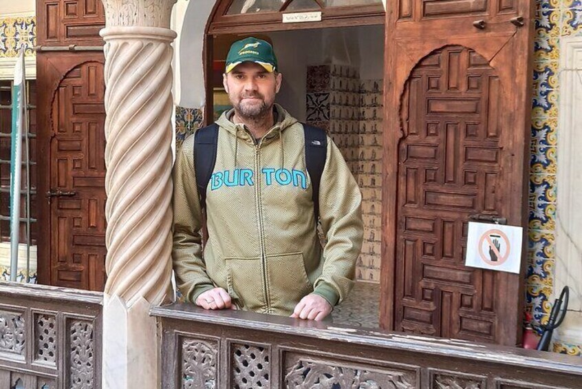 A person standing at a wooden door with intricate carvings, wearing a green jacket with 'BUR TON' text, and a backpack. 3