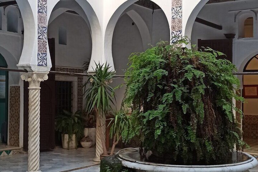 A courtyard with arches, a central fountain, and potted plants. 2