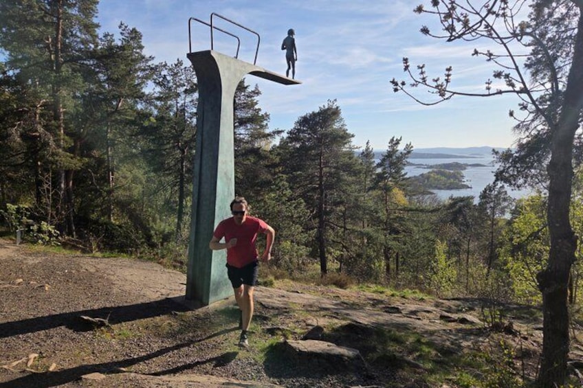 A person running on a trail with a large metal structure and a body of water in the background. 1