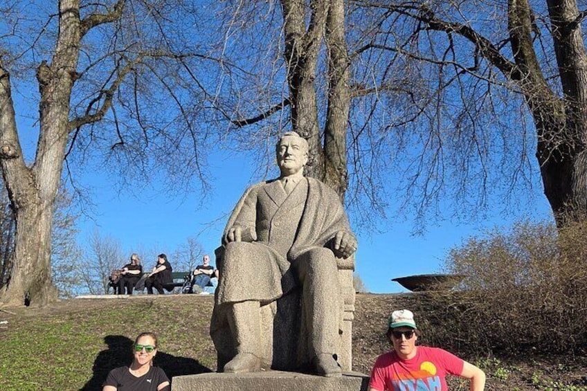 A statue of a seated figure in a park with trees and a clear sky in the background. 3