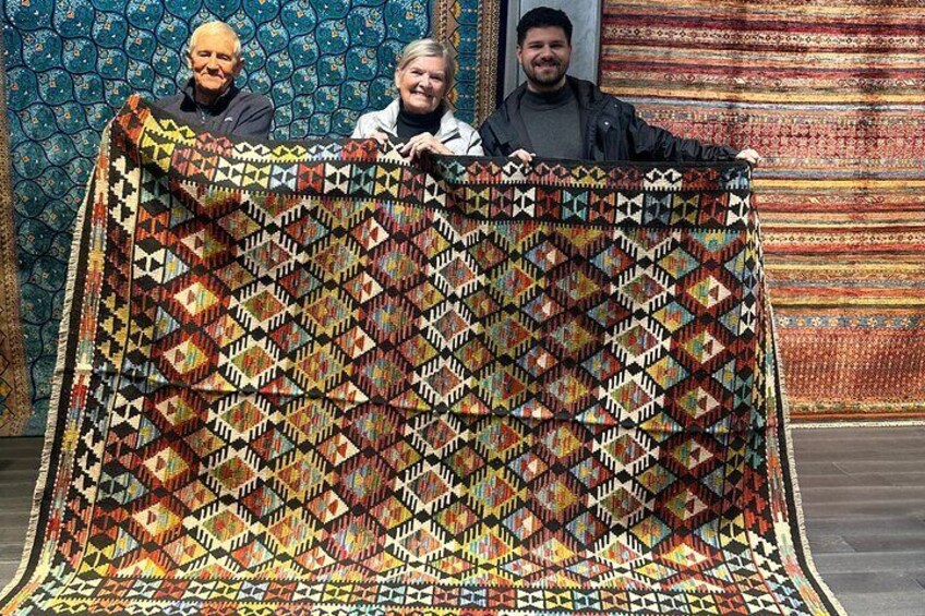 Three people holding a colorful quilt with a geometric pattern. 5