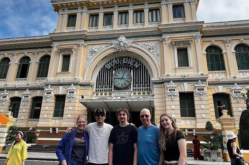A group of people standing in front of a historic building with ornate architecture and a large clock. 1