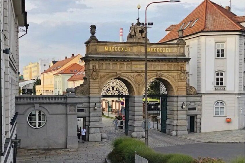 A historic archway with inscriptions, a cobblestone street, and traditional buildings. 2