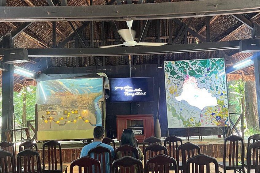 An indoor presentation area with a map, a screen, and chairs arranged for an audience. 3