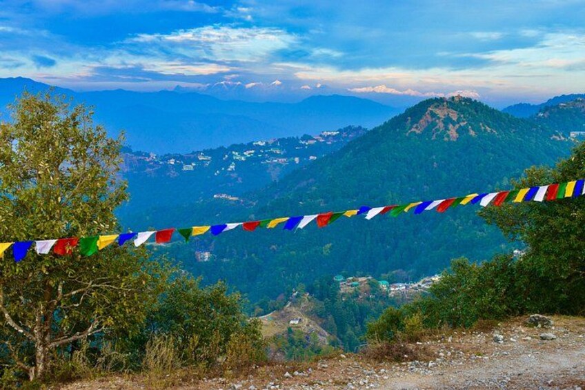 A mountainous landscape with a colorful prayer flag line, trees, and distant buildings. 3