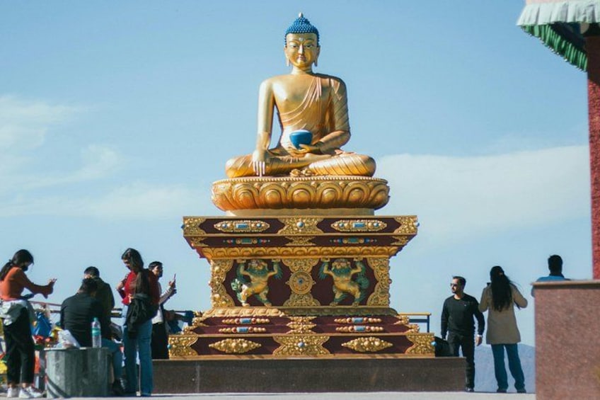 A large golden Buddha statue on a multi-tiered pedestal with intricate designs, surrounded by people. 4