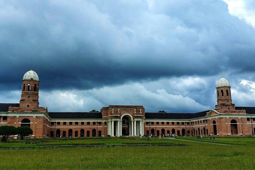 A large brick building with two towers and a central dome, surrounded by a green field. 5