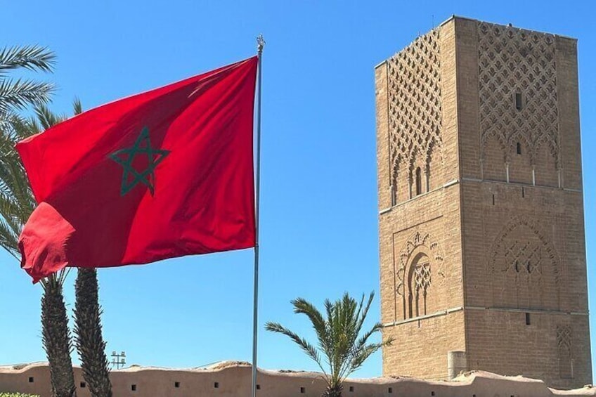 A flag with a green star and crescent, a tall tower with intricate patterns, and palm trees in the background. 1