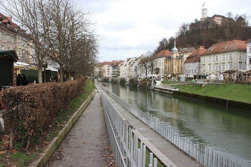 A river with buildings on the right bank, a pathway on the left, and a hill with a tower in the background. 5