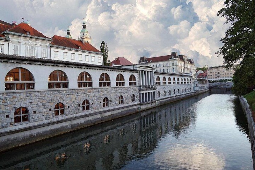 A canal with buildings on one side, a bridge in the distance, and a cloudy sky. 4