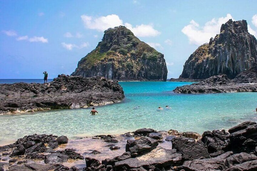 A rocky beach with clear turquoise water and two prominent rock formations in the background. 5
