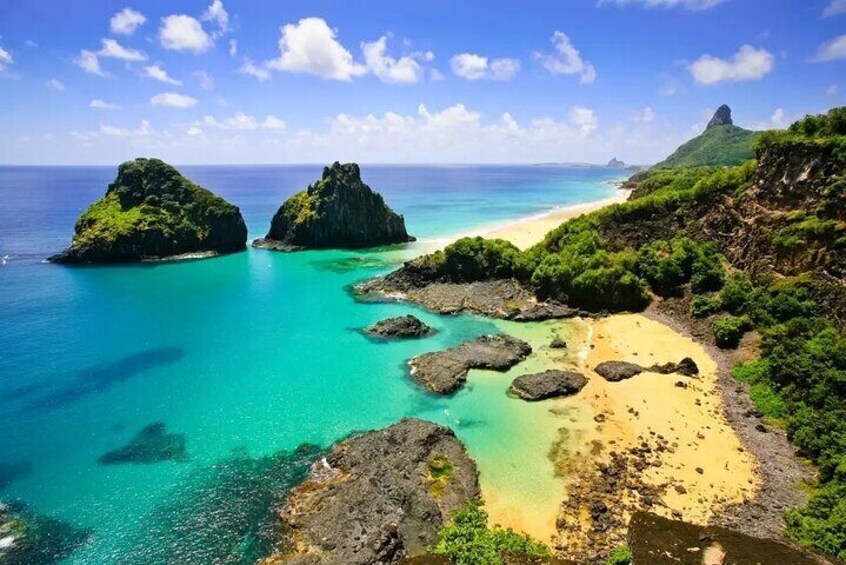 A coastal landscape with clear turquoise waters, rocky outcrops, and a sandy beach. 1