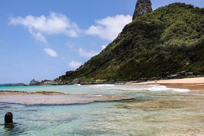 A beach with clear turquoise water, a sandy shore, and a green hill with a tall rock formation. 2