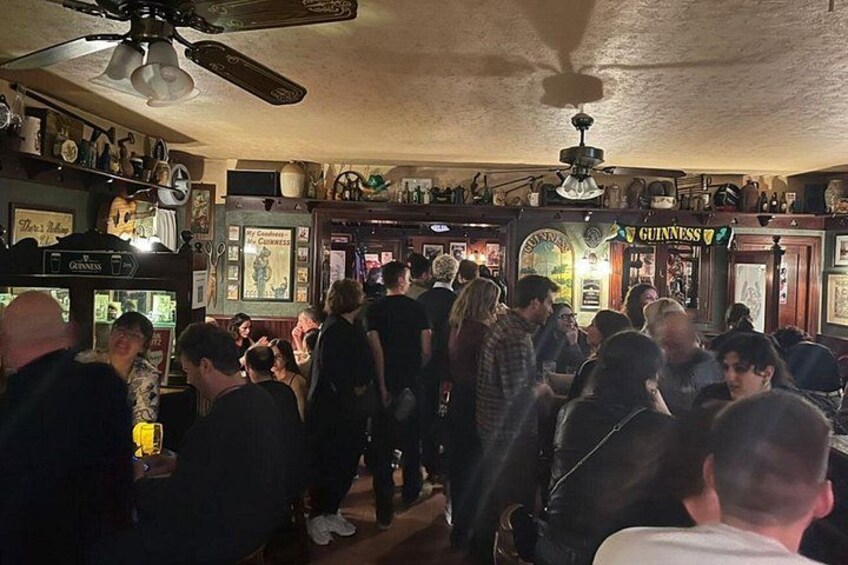 A crowded bar with Guinness signage, ceiling fans, and various memorabilia on the walls. 3