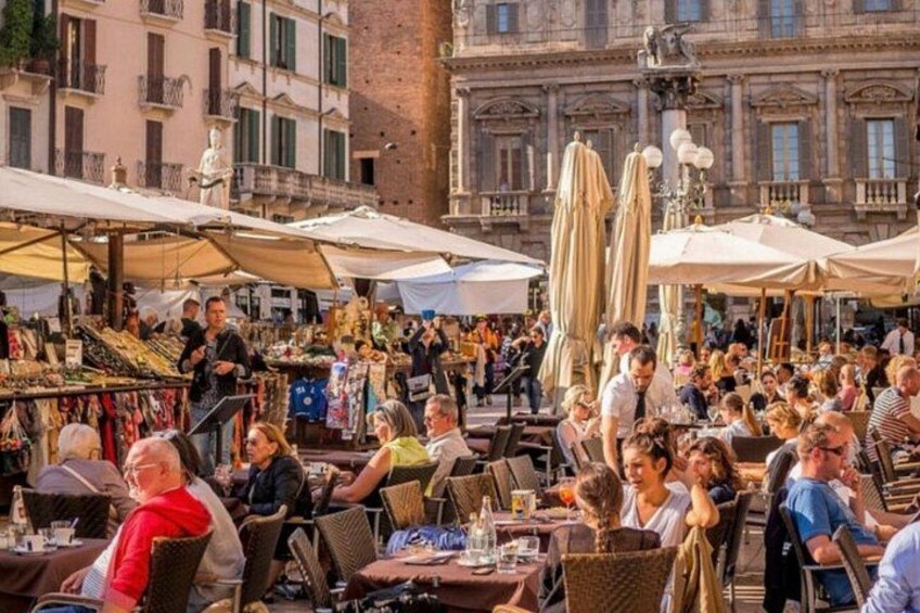 A crowded outdoor market with tables and umbrellas, surrounded by historic buildings. 4