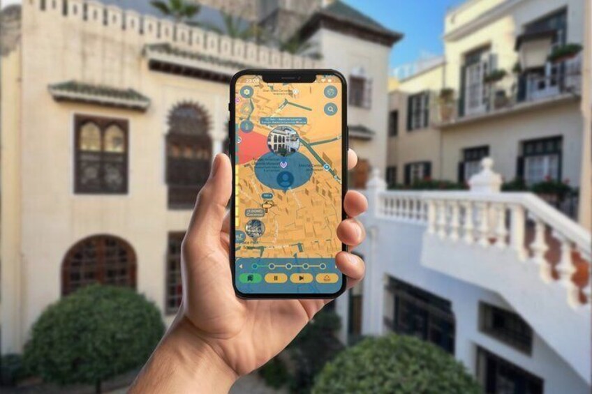 A hand holding a smartphone displaying a map with a highlighted area, in front of a building with arched windows and balconies. 1