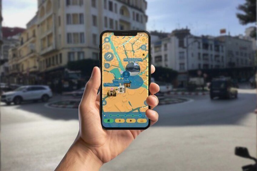 A hand holding a smartphone displaying a map with a blue icon, a roundabout, and buildings in the background. 3