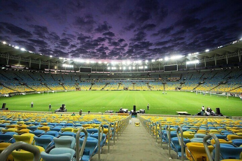 A stadium with empty blue and yellow seats, a green field, and a purple sky. 1