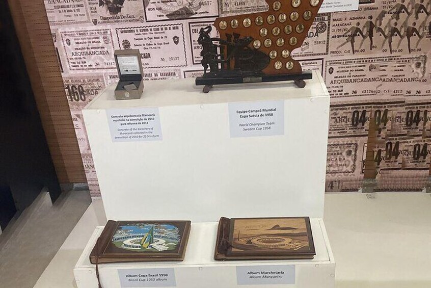A display of trophies and memorabilia, including a World Champion trophy and a medal, on a white pedestal with a backdrop of historical documents. 4
