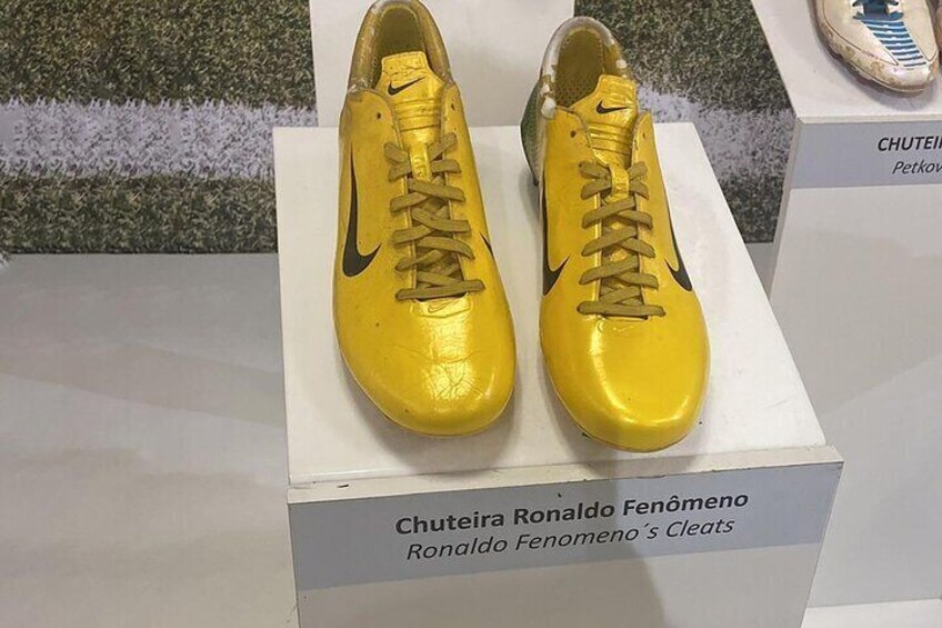 A pair of yellow soccer cleats on display with a sign reading "Chuteira Ronaldo Fenomeno Ronaldo Fenomeno's Cleats". 5