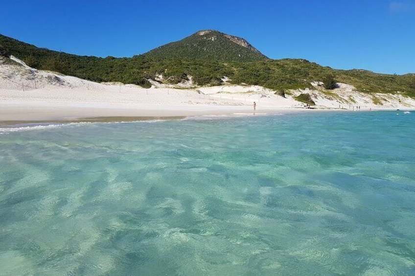 A beach with clear turquoise water, white sand, and a green hill in the background. 1