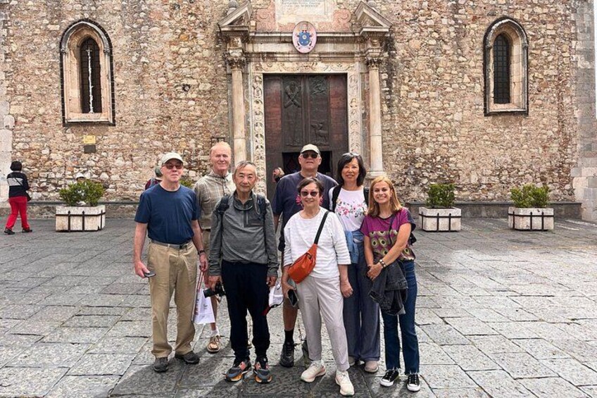 A group of people standing in front of a stone building with arched windows and a door. 3