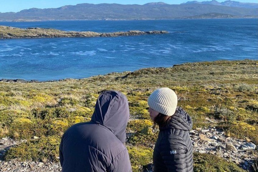 Two people sitting on a rocky outcrop overlooking a body of water with distant mountains. 3