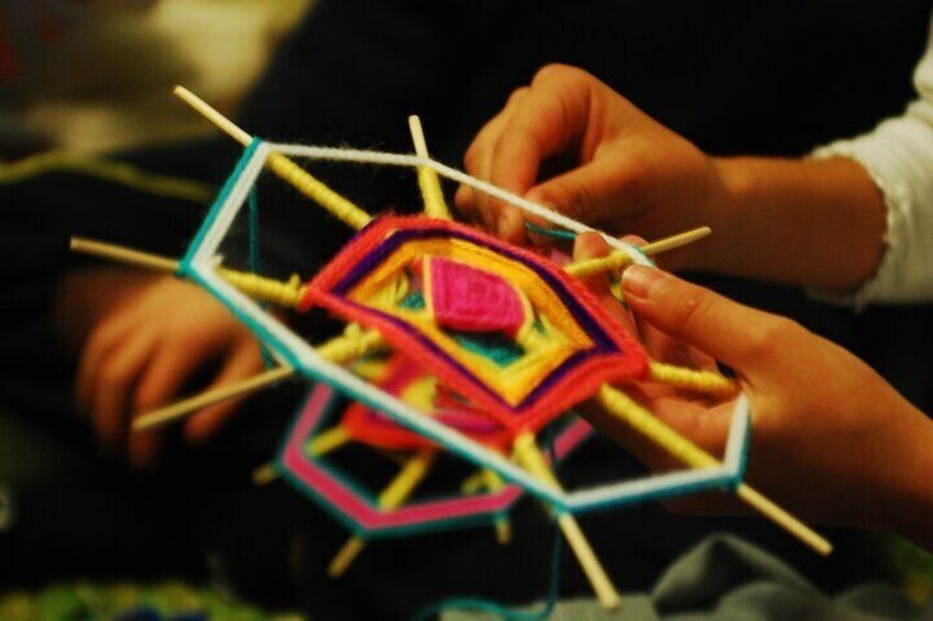 Hands weaving a colorful geometric pattern with sticks. 4