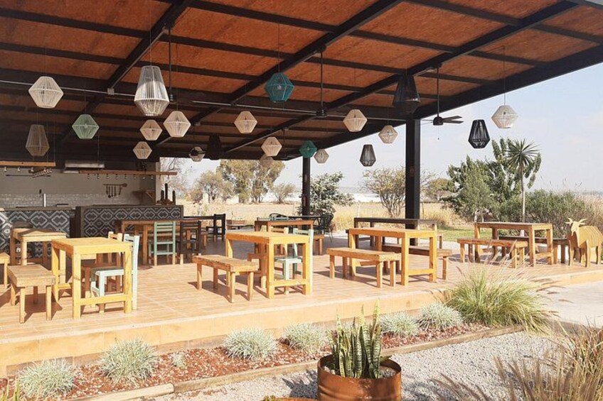 An outdoor seating area with wooden tables and chairs, hexagonal hanging lights, and a view of the landscape. 4