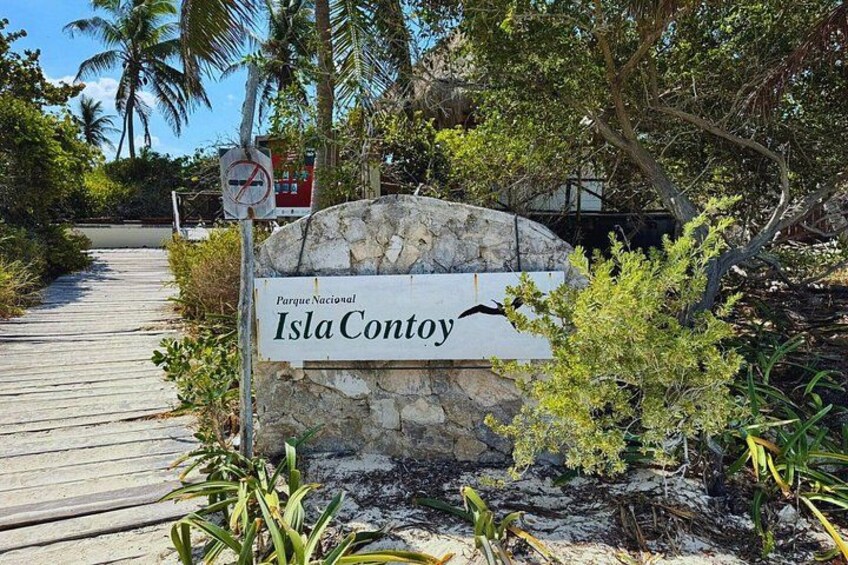 A sign for Parque Nacional Isla Contoy with a wooden walkway and tropical vegetation. 3
