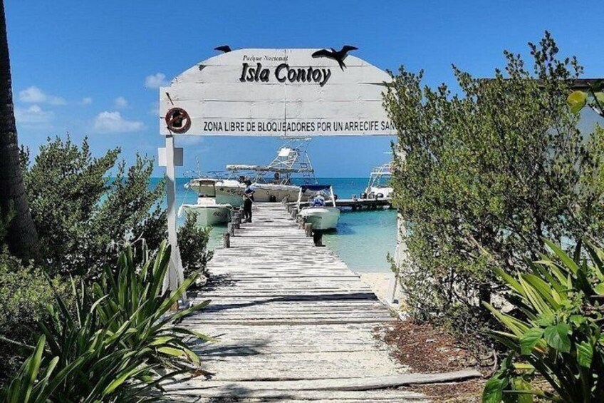 A wooden dock leading to Isla Contoy with boats docked and a sign indicating a free zone. 5