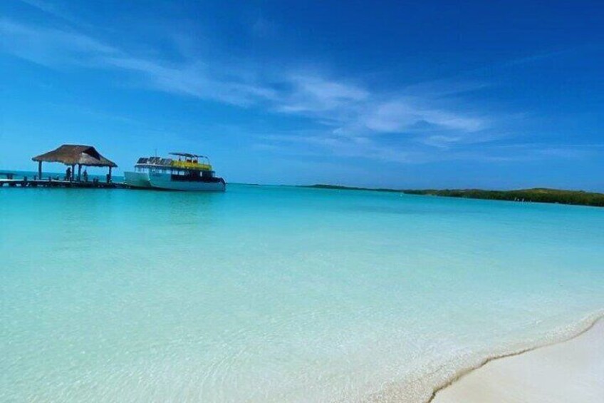 A clear turquoise sea, a boat, and a beach with a hut. 1