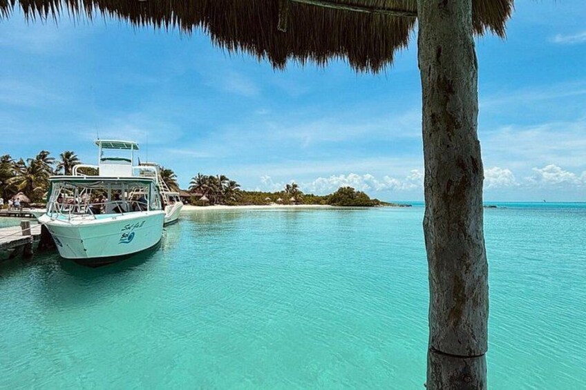 A boat docked at a pier, clear turquoise water, and a small island with palm trees in the background. 4