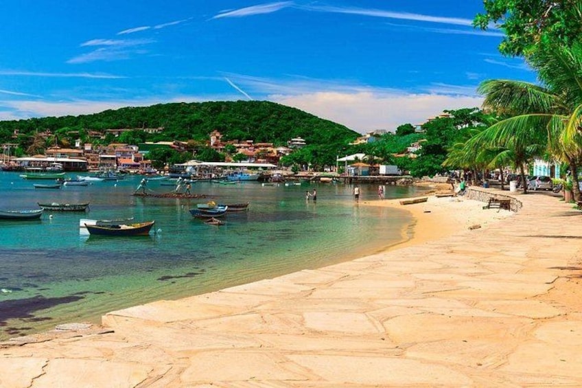 A beach with clear water, boats, and a hillside with buildings. 1
