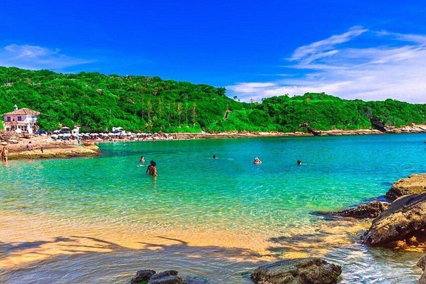 A beach with clear turquoise water, rocky shoreline, and lush green hills in the background. 3