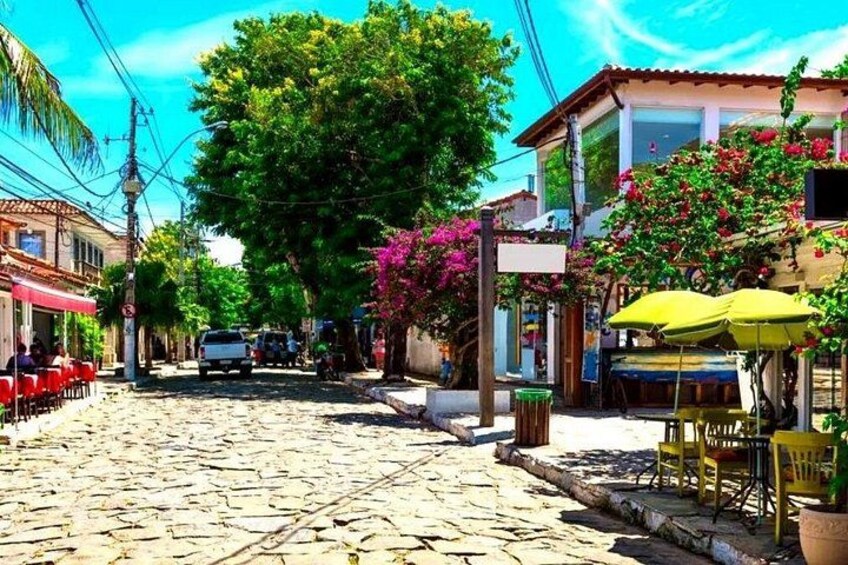 A cobblestone street lined with colorful buildings, a parked car, and a tree with pink flowers. 4