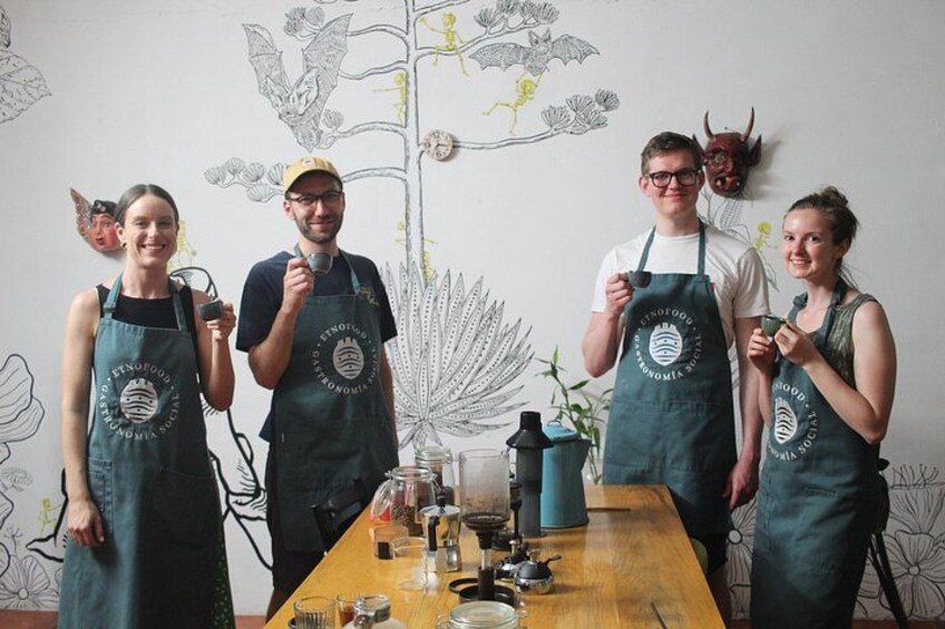 A group of people standing around a table with aprons, a plant, and a wall with a drawing. 1