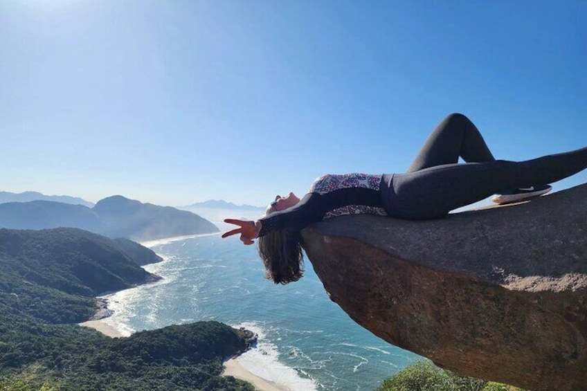 A person lying on a rock overlooking a coastal landscape with mountains and a beach. 3