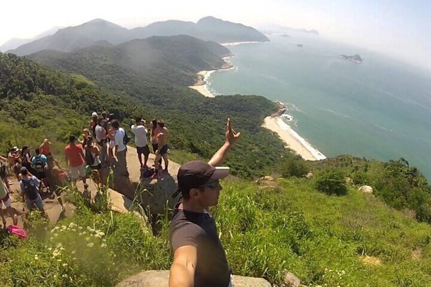 A group of people on a hiking trail overlooking a coastal landscape with mountains and a beach. 4