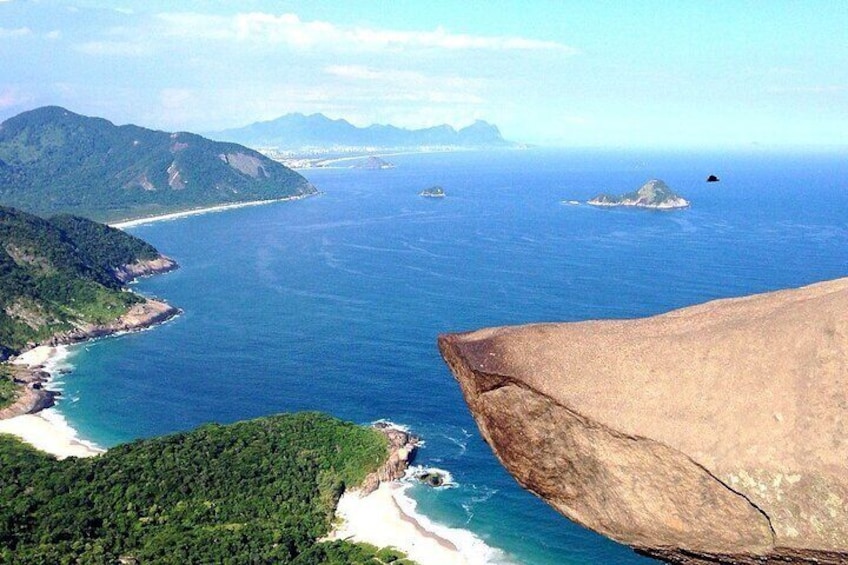 A coastal landscape with a large rock formation, a beach, and a clear view of the ocean. 2