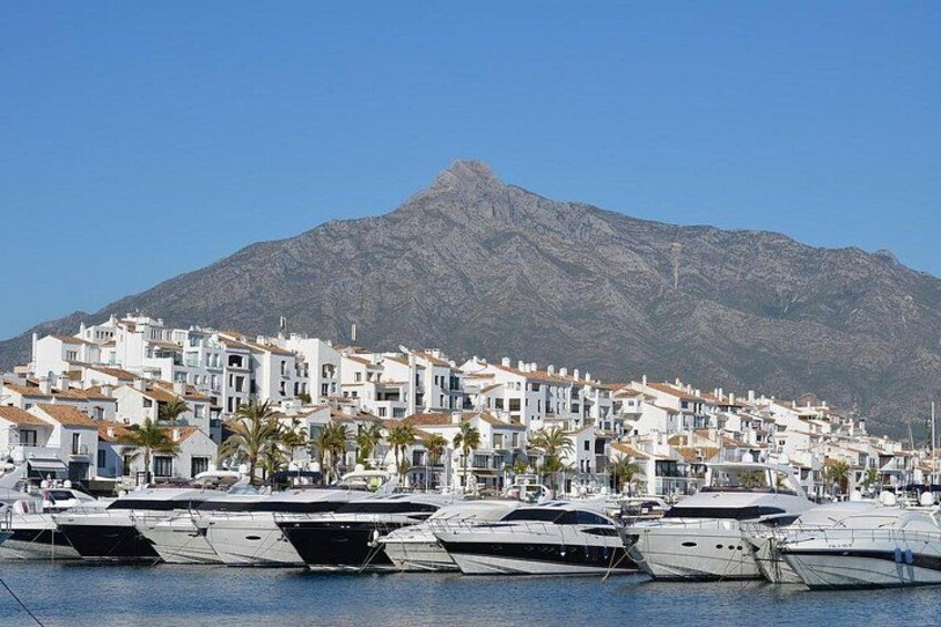 Un puerto deportivo con yates, un pueblo costero con edificios blancos y una montaña al fondo. 4