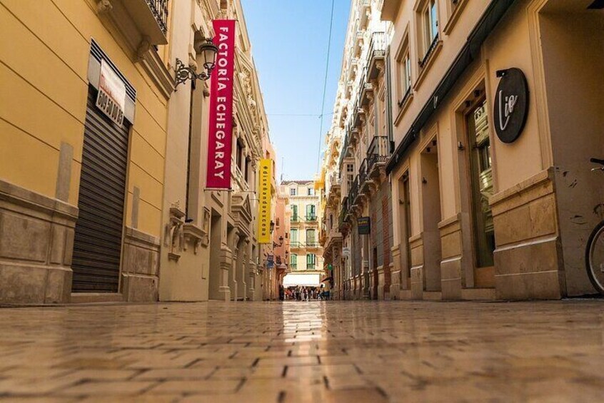 A narrow street with buildings on either side, a closed shutter on the left, and a sign for 'FACTORIA ECHIGARAY' on the right. 3