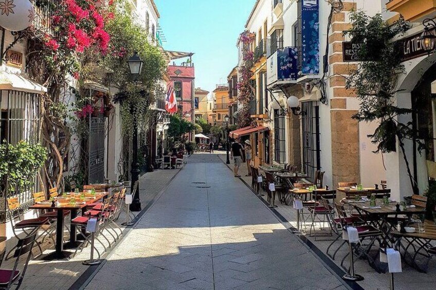A narrow street lined with outdoor cafes, tables, and chairs, with buildings on either side. 5