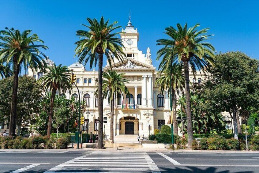 A grand building with a clock tower, surrounded by palm trees and a crosswalk. 2