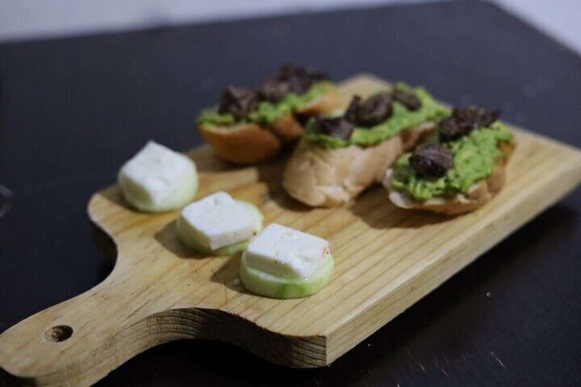 A wooden board with three pieces of food, two with green toppings and one with white. 5
