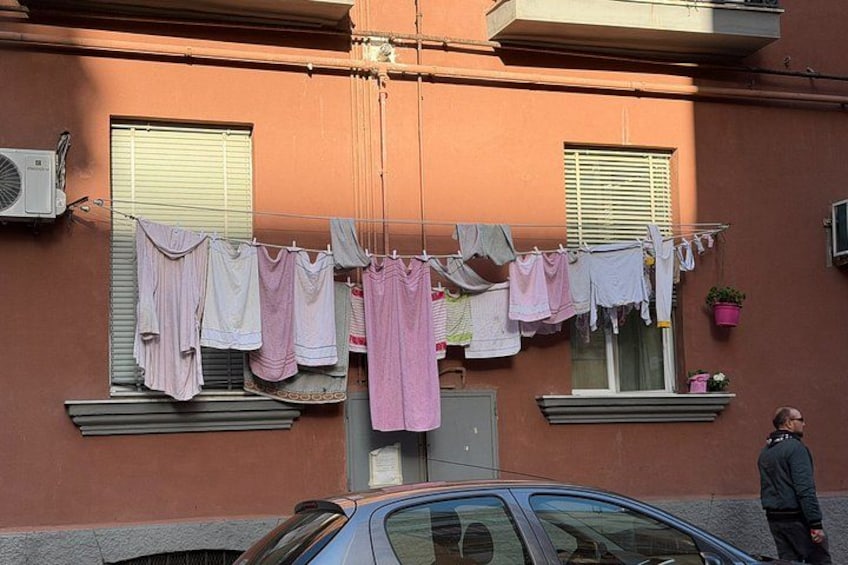 A building with laundry hanging on a clothesline, a parked car, and a person standing nearby. 5