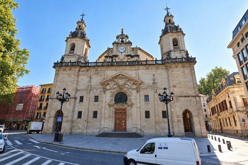 A historic church with two bell towers, a large central entrance, and a clock. 1