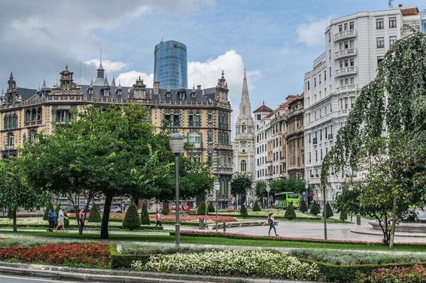 A city square with historic buildings, a modern skyscraper, and well-maintained gardens. 1